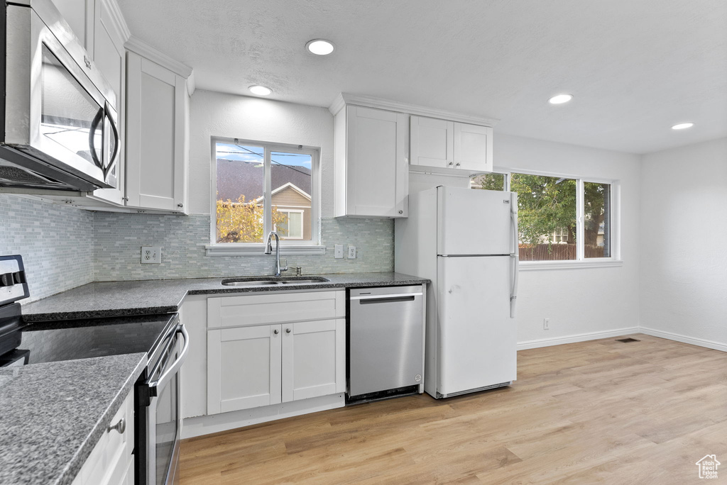 Kitchen with sink, backsplash, light hardwood / wood-style floors, stainless steel appliances, and white cabinets