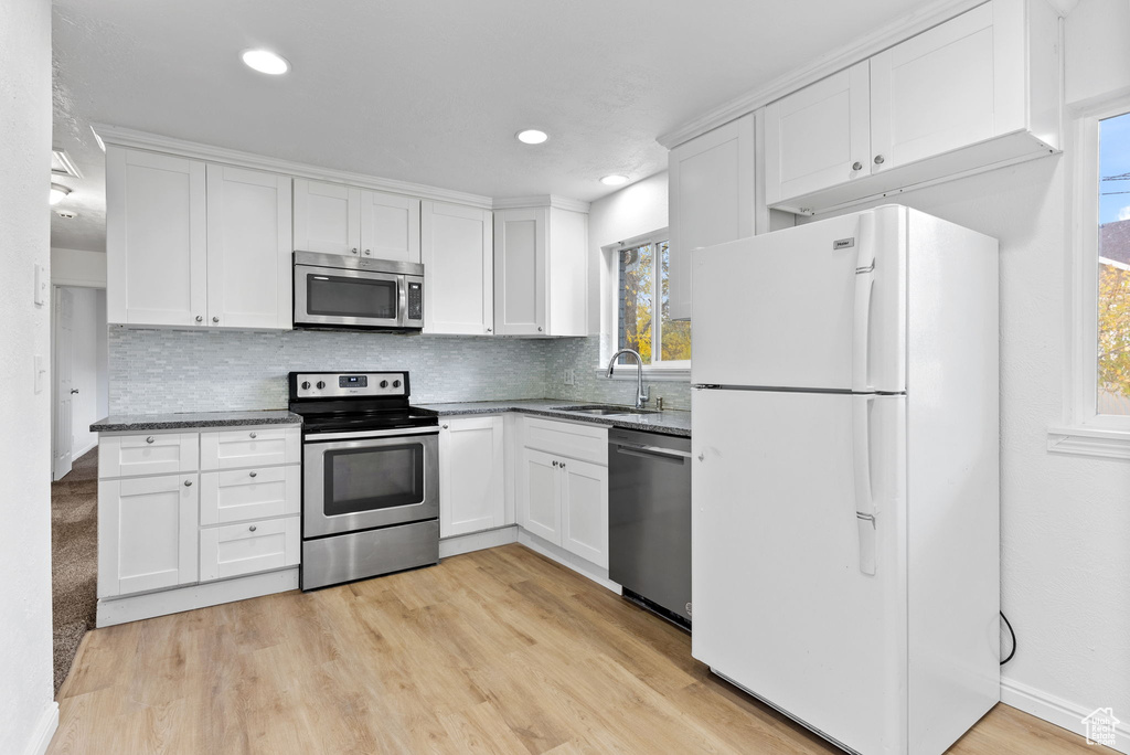 Kitchen with sink, white cabinetry, stainless steel appliances, and light wood-type flooring