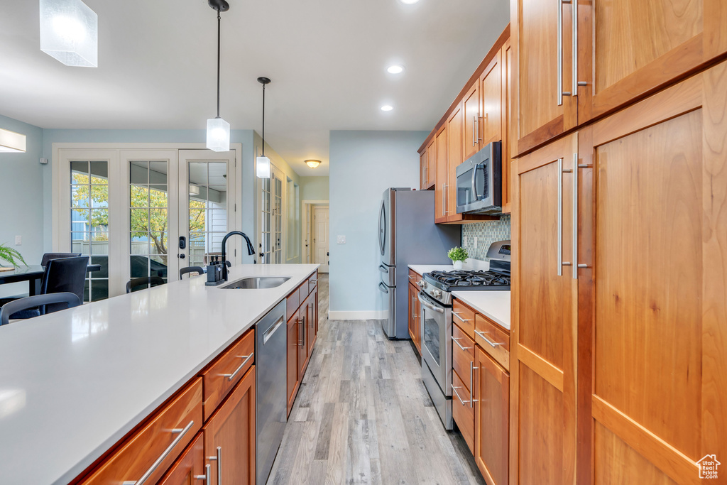 Kitchen featuring hanging light fixtures, a sink, light wood-style floors, light countertops, and stainless steel appliances