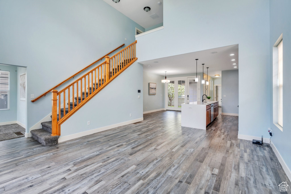 Unfurnished living room featuring baseboards, a high ceiling, wood finished floors, and stairway