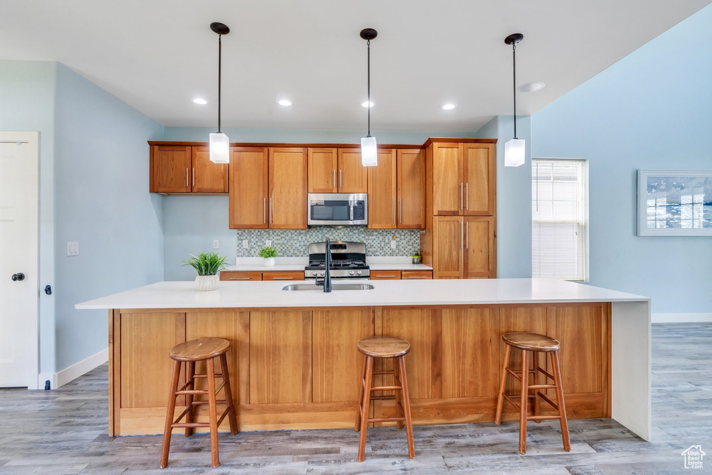 Kitchen featuring brown cabinets, a sink, light countertops, stainless steel appliances, and backsplash