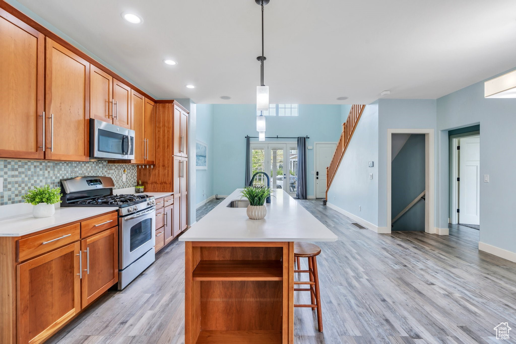 Kitchen with a sink, a kitchen island with sink, french doors, stainless steel appliances, and decorative backsplash