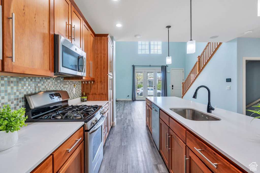 Kitchen with appliances with stainless steel finishes, a sink, light countertops, decorative backsplash, and wood finished floors