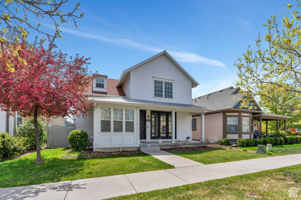 View of front of home with covered porch, fence, metal roof, and a front yard