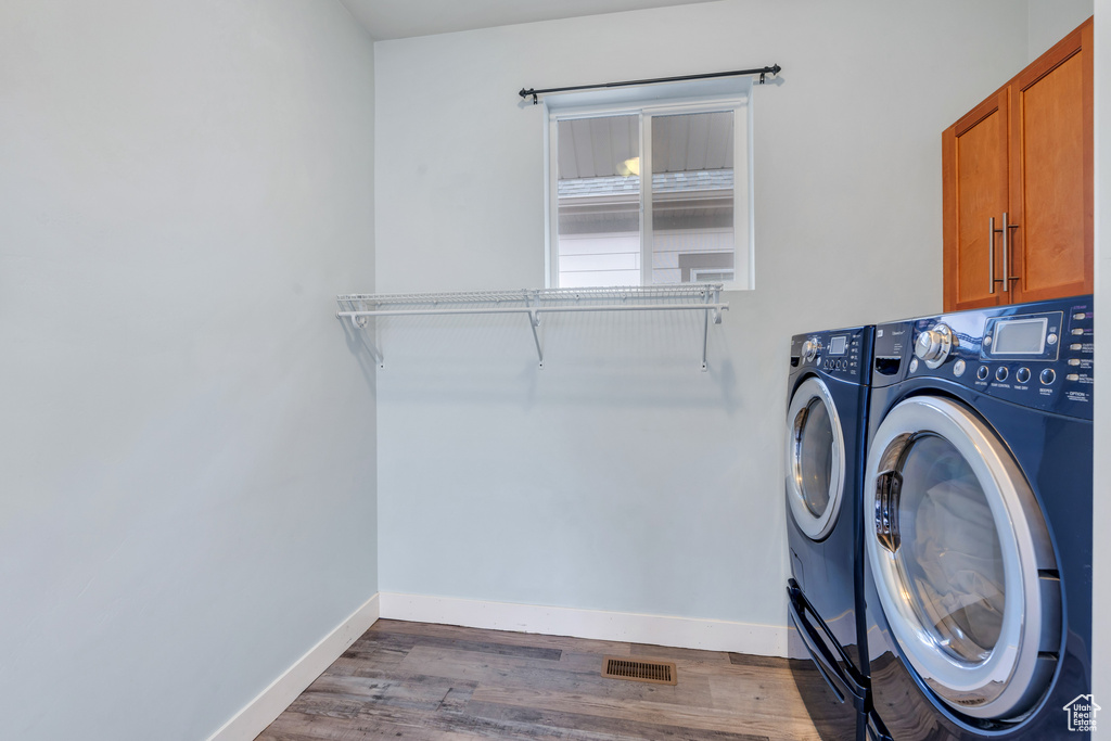 Laundry room featuring cabinet space, separate washer and dryer, baseboards, wood finished floors, and visible vents