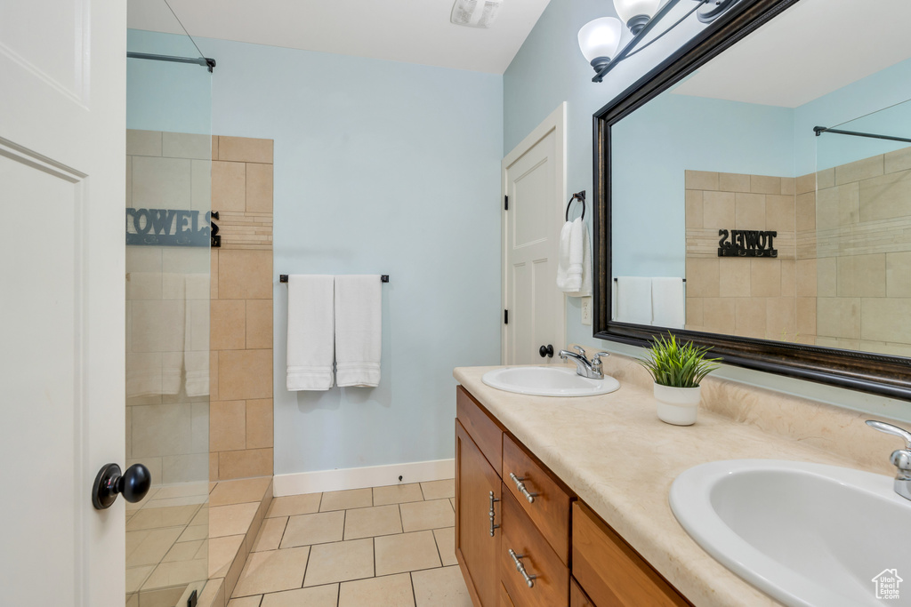 Bathroom with tile patterned flooring, a sink, a tile shower, and double vanity