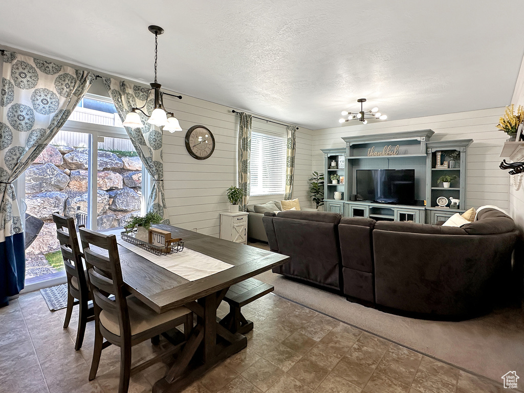 Dining space with a notable chandelier, a healthy amount of sunlight, a textured ceiling, and wood walls