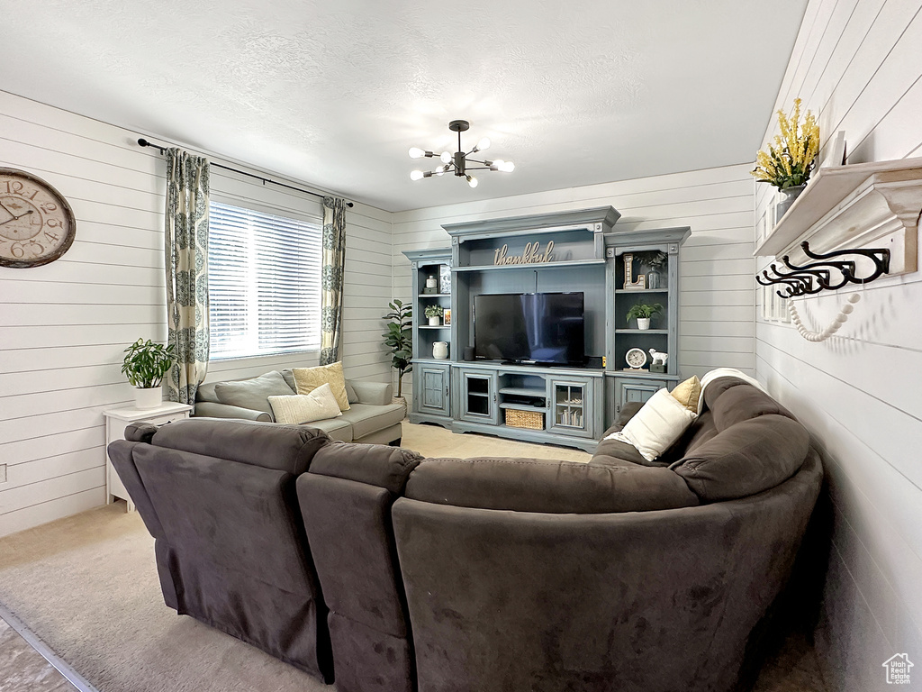 Carpeted living room with a textured ceiling, a chandelier, and wooden walls