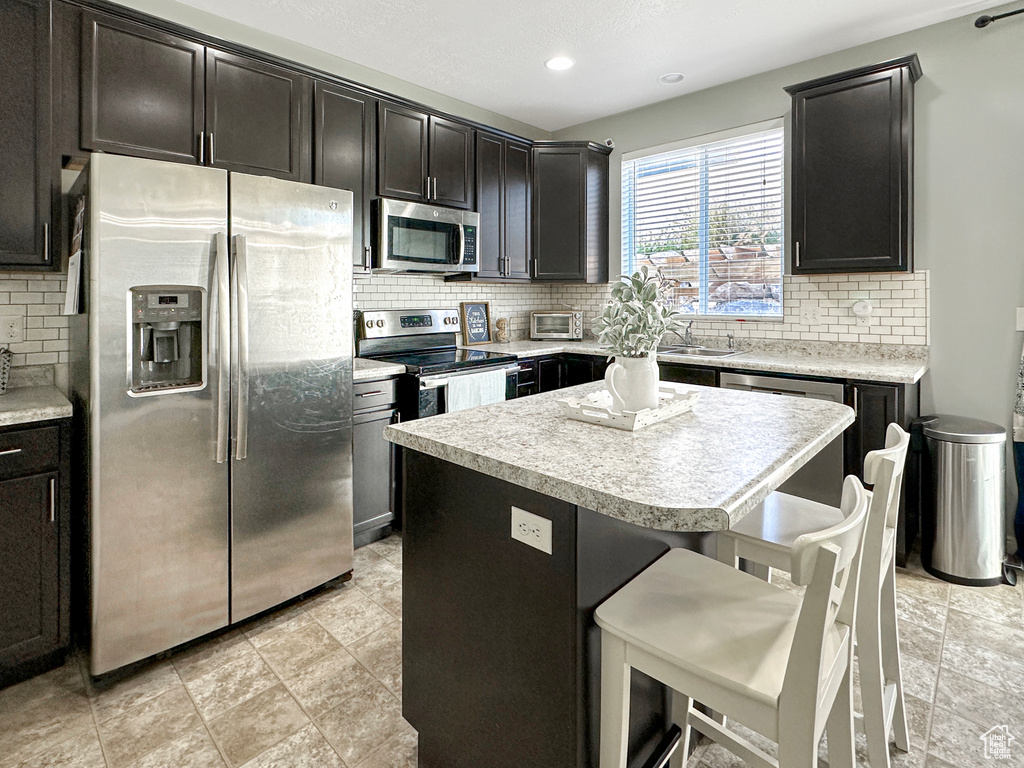 Kitchen featuring appliances with stainless steel finishes, sink, a center island, decorative backsplash, and a breakfast bar area