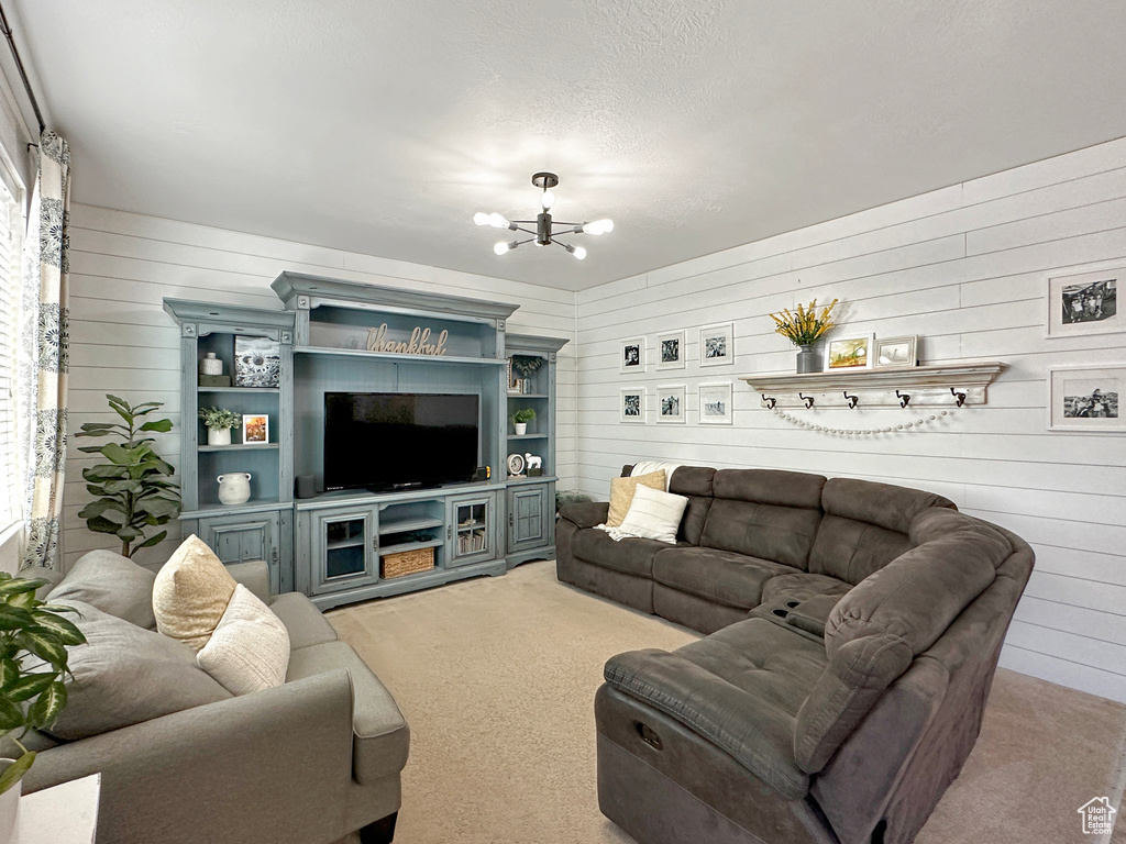 Carpeted living room with a notable chandelier, wooden walls, and a wealth of natural light