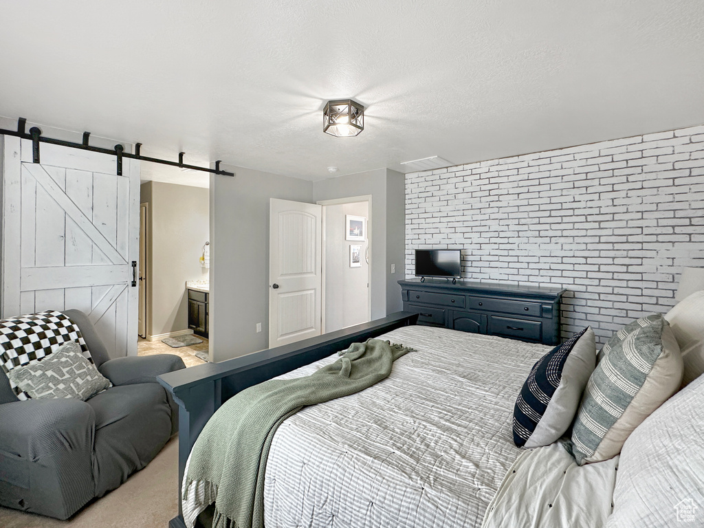 Bedroom with light carpet, a textured ceiling, a barn door, ensuite bathroom, and brick wall