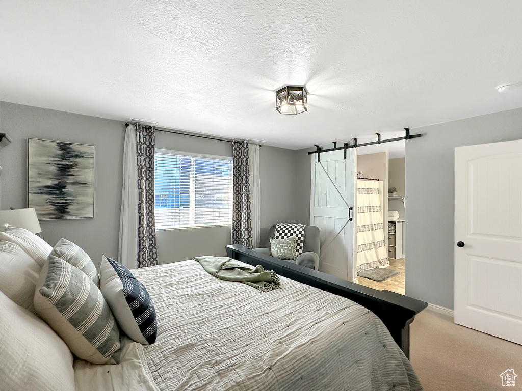 Bedroom with connected bathroom, a textured ceiling, a barn door, and carpet floors