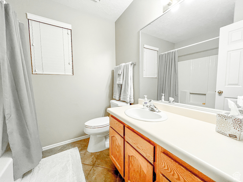 Full bathroom featuring a textured ceiling, toilet, tile patterned floors, vanity, and shower / bathtub combination with curtain