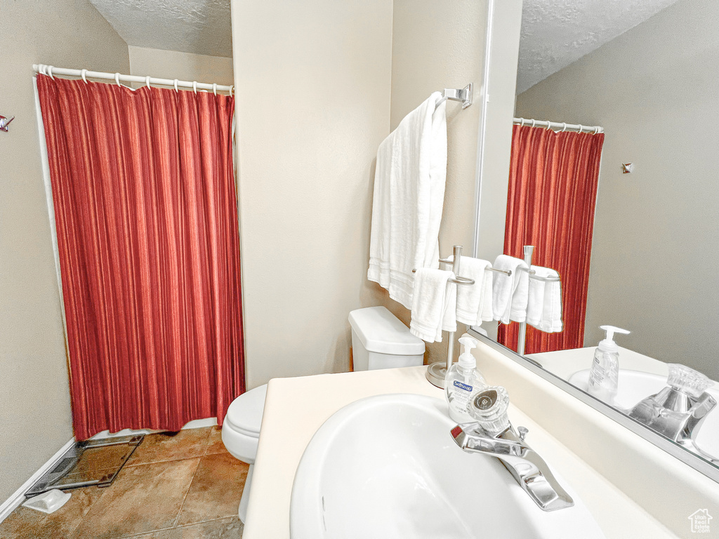 Bathroom with toilet, a textured ceiling, and tile patterned flooring