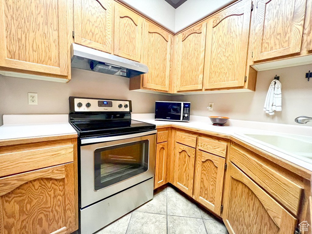 Kitchen with light brown cabinets, stainless steel electric range, light tile patterned floors, and extractor fan