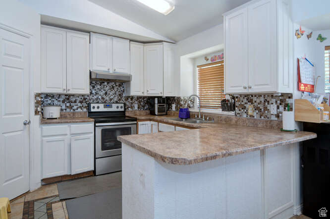 Kitchen with a wealth of natural light, white cabinets, kitchen peninsula, and stainless steel range with electric cooktop