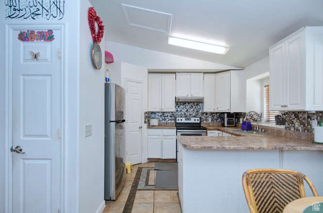 Kitchen featuring kitchen peninsula, lofted ceiling, backsplash, white cabinetry, and stainless steel appliances