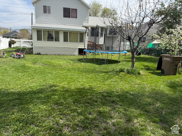 Rear view of property featuring fence, a trampoline, and a lawn
