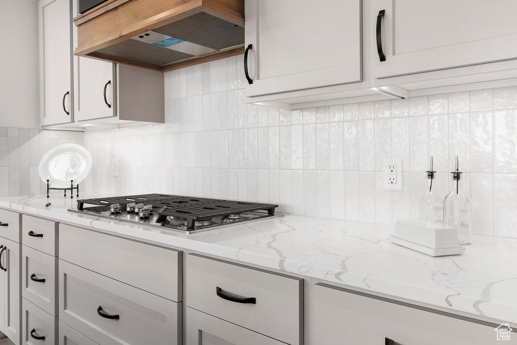 Kitchen with tasteful backsplash, extractor fan, light stone countertops, and stainless steel gas stovetop