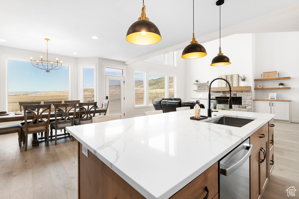 Kitchen featuring a kitchen island with sink, a sink, light wood-type flooring, dishwasher, and pendant lighting