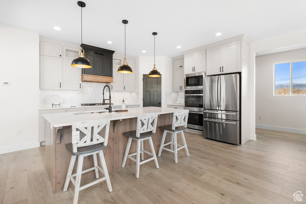 Kitchen featuring a kitchen island with sink, a breakfast bar, appliances with stainless steel finishes, light wood finished floors, and tasteful backsplash