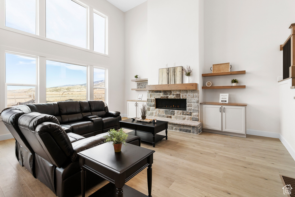 Living room featuring light wood-type flooring, baseboards, a stone fireplace, and a high ceiling