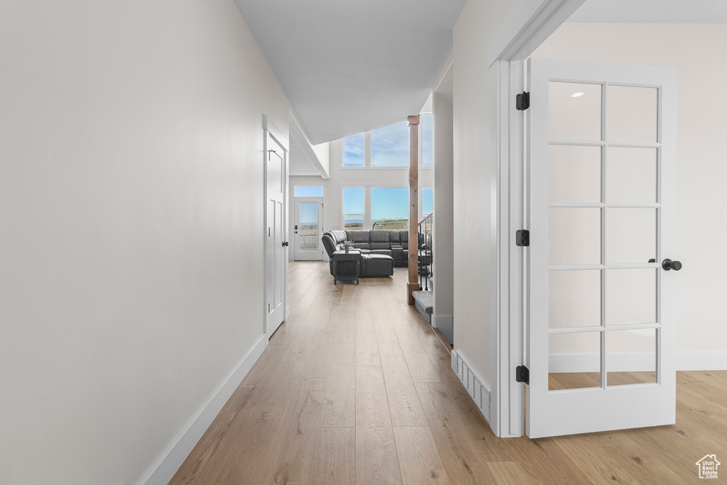 Corridor featuring high vaulted ceiling, baseboards, and light wood finished floors