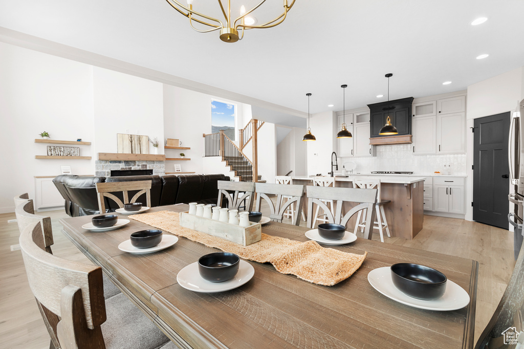 Dining room with a fireplace, light wood-style flooring, an inviting chandelier, and stairs