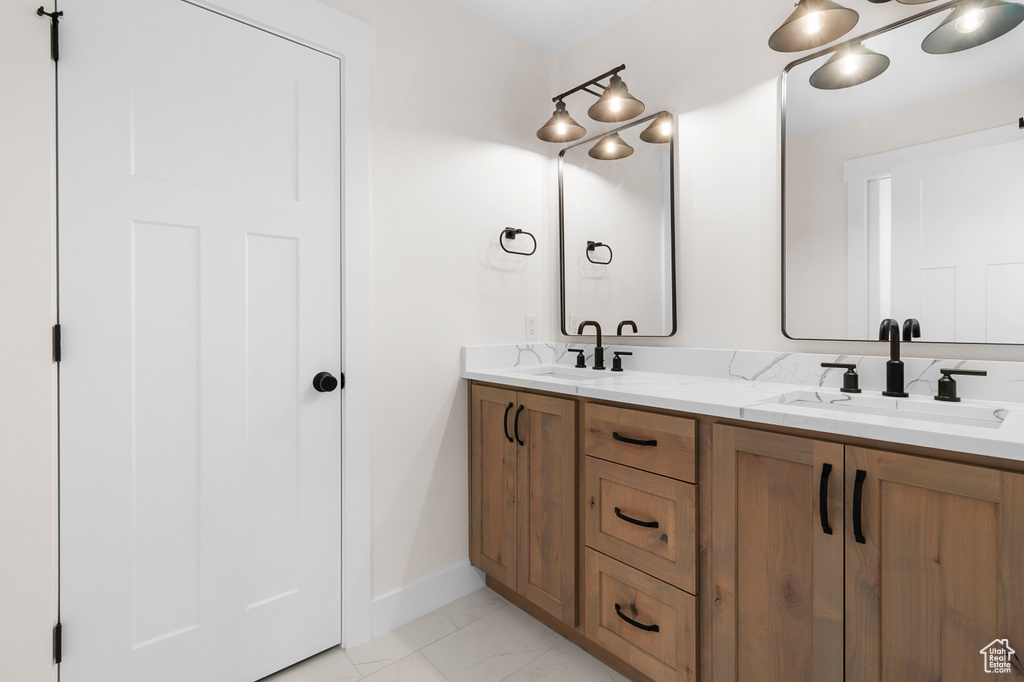 Full bath with marble finish floor, double vanity, a sink, and baseboards