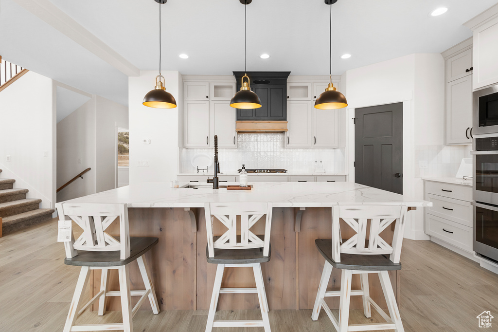 Kitchen featuring light stone counters, tasteful backsplash, a center island with sink, and light wood-style floors