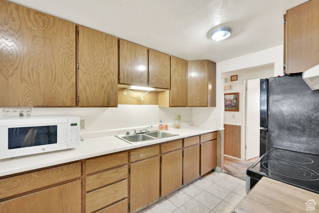 Kitchen with light tile patterned flooring, black appliances, and sink