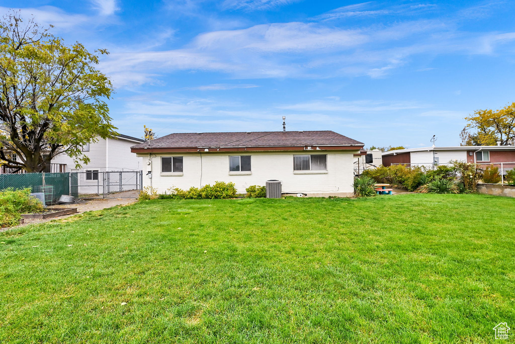 Back of house with central air condition unit and a lawn