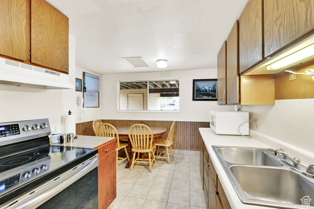 Kitchen with sink, electric range, light tile patterned floors, and wood walls