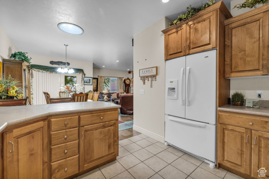 Kitchen with hanging light fixtures, white refrigerator with ice dispenser, and light tile patterned floors