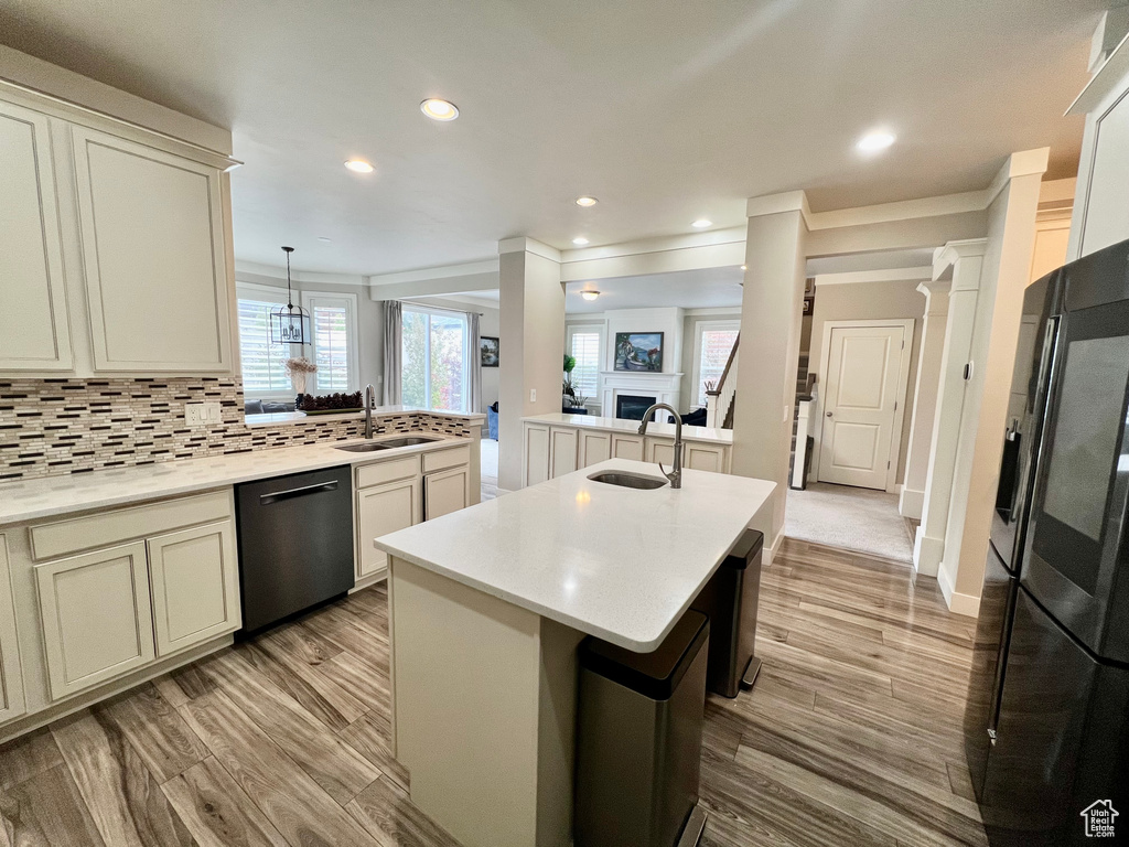 Kitchen with dishwasher, black refrigerator, a center island with sink, sink, and decorative light fixtures