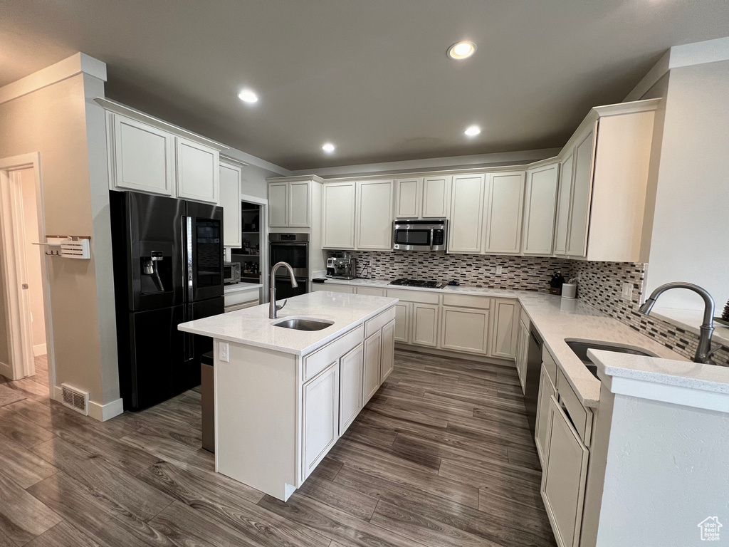 Kitchen with sink, black appliances, a kitchen island with sink, and dark hardwood / wood-style flooring