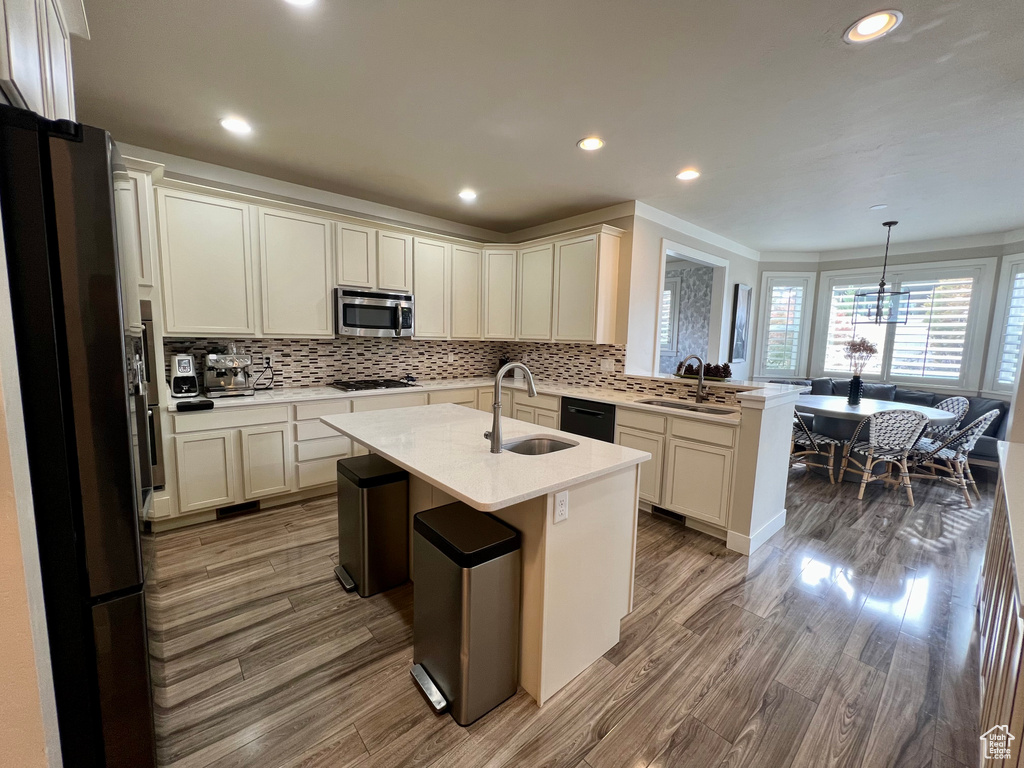 Kitchen featuring a kitchen island with sink, wood-type flooring, sink, decorative light fixtures, and appliances with stainless steel finishes