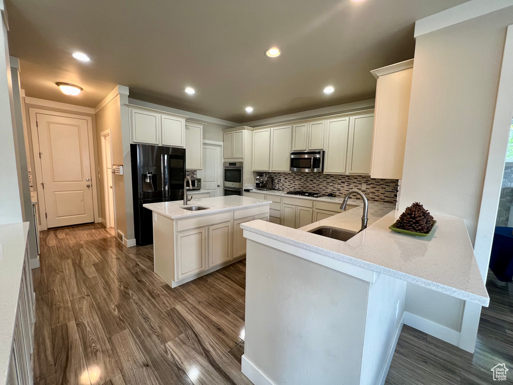 Kitchen featuring kitchen peninsula, a center island with sink, sink, black appliances, and dark hardwood / wood-style flooring