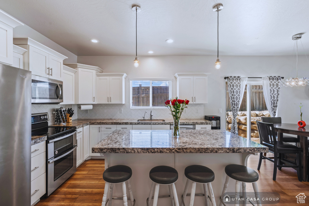 Kitchen with appliances with stainless steel finishes, sink, a center island, white cabinets, and dark hardwood / wood-style floors