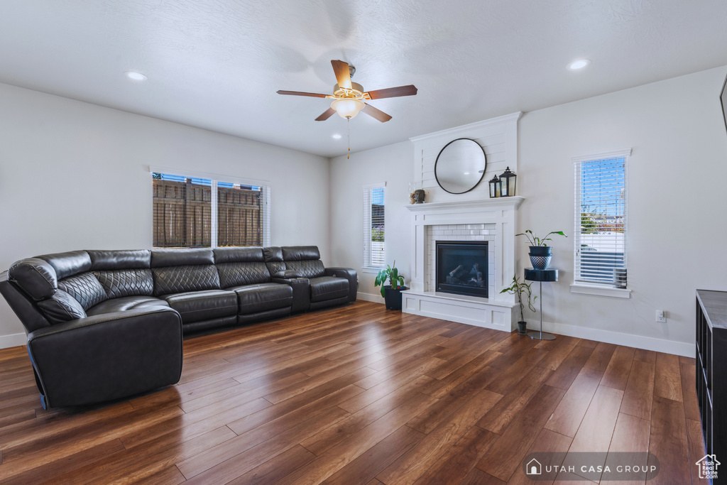 Living room featuring a tiled fireplace, ceiling fan, plenty of natural light, and dark hardwood / wood-style flooring