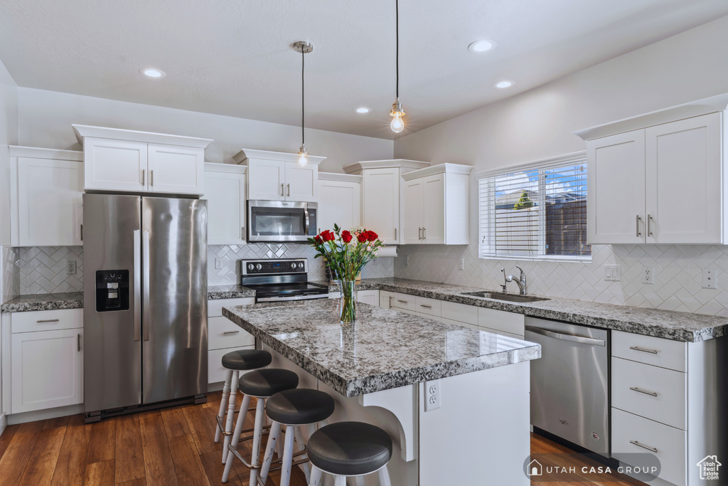 Kitchen featuring a kitchen island, hanging light fixtures, white cabinets, appliances with stainless steel finishes, and dark hardwood / wood-style flooring