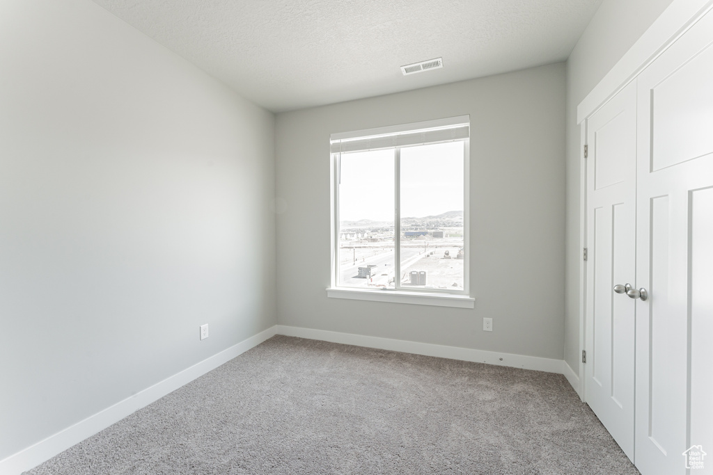 Unfurnished bedroom featuring baseboards, a textured ceiling, visible vents, and carpet