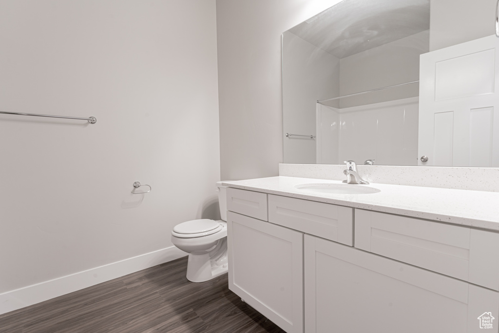 Bathroom featuring walk in shower, baseboards, toilet, wood finished floors, and vanity