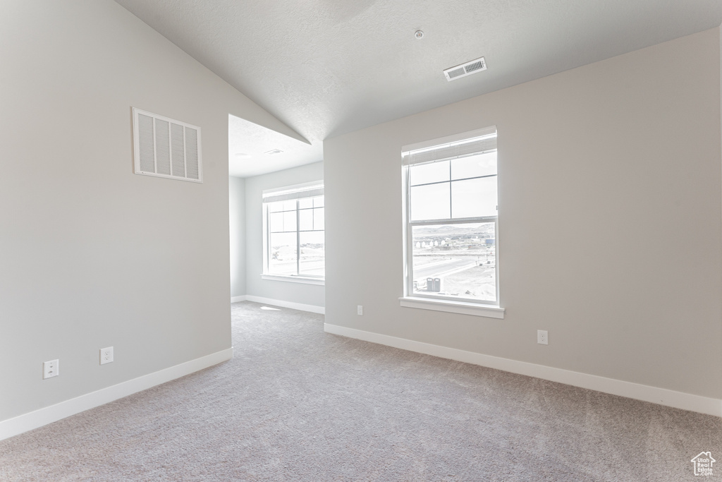 Carpeted spare room featuring baseboards, a textured ceiling, visible vents, and vaulted ceiling