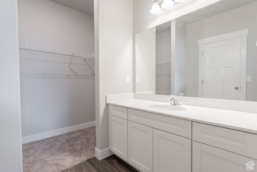 Bathroom with baseboards, wood finished floors, a spacious closet, and vanity