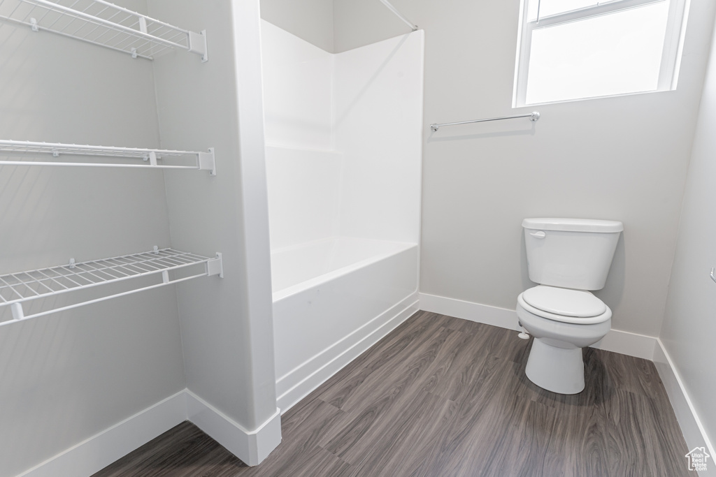 Full bathroom featuring baseboards, wood finished floors, toilet, and shower / bathtub combination