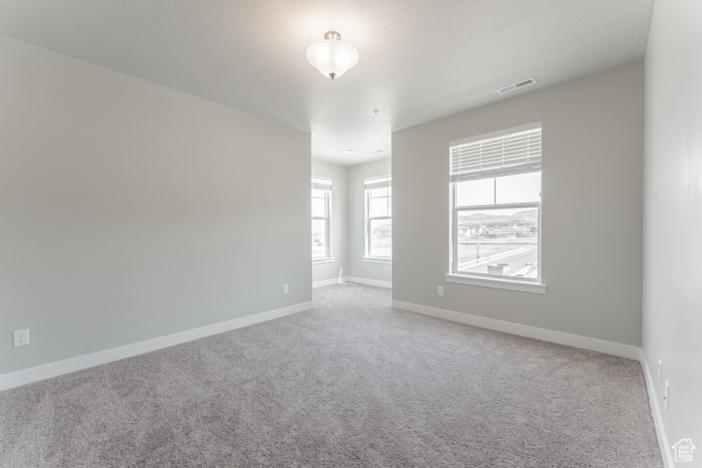 Unfurnished room featuring baseboards, visible vents, and light colored carpet