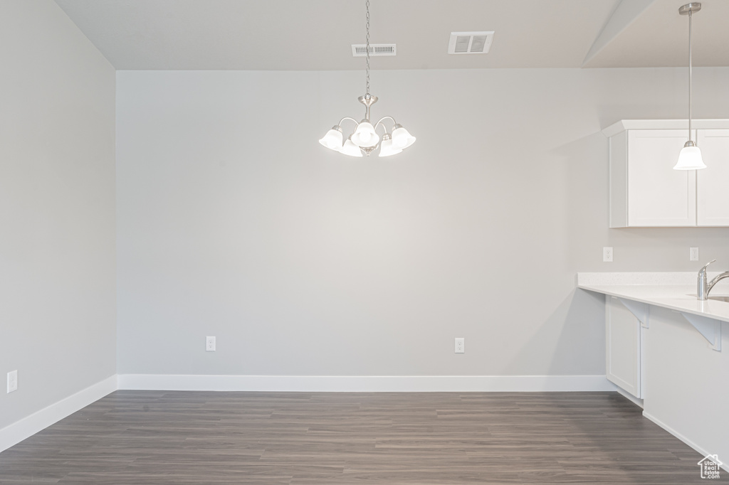 Unfurnished dining area featuring dark wood finished floors, a notable chandelier, and visible vents