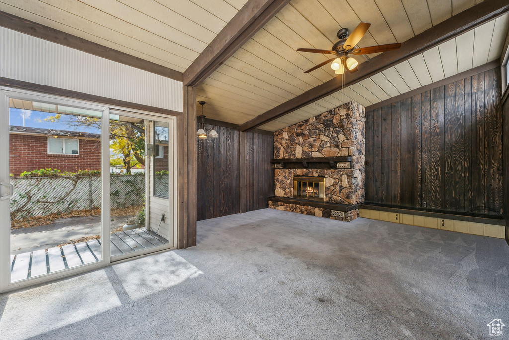 Unfurnished living room featuring lofted ceiling with beams, a stone fireplace, carpet flooring, and wood walls