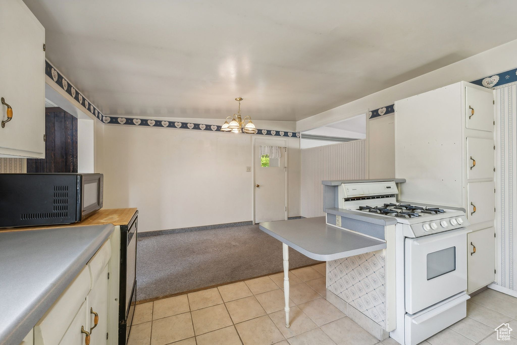 Kitchen featuring light tile patterned flooring, white range with gas stovetop, hanging light fixtures, white cabinetry, and a notable chandelier